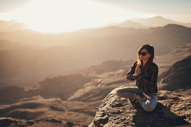 Mujer se sienta en una pose de yoga en el Monte Sinaí y medita sobre el fondo de la salida del sol
. - Foto, imagen