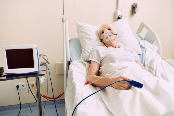 Retired lady lying in hospital bed with respiratory support - Valokuva, kuva