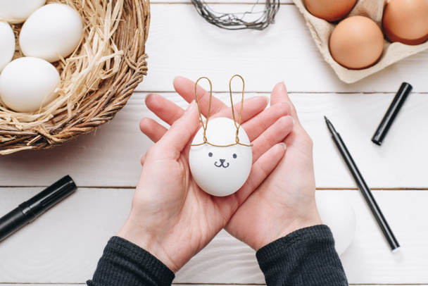 обрезанное изображение женщины, держащей куриное пасхальное яйцо с кроличьими ушами и улыбкой
 - Фото, изображение