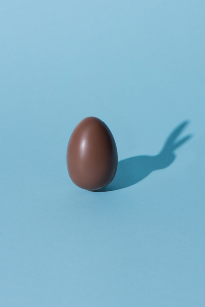 un oeuf de Pâques en chocolat avec ombre de lapin sur la surface bleue
 - Photo, image
