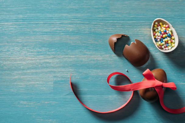 вид разбитых пасхальных яиц из шоколада на бирюзовом столе
 - Фото, изображение