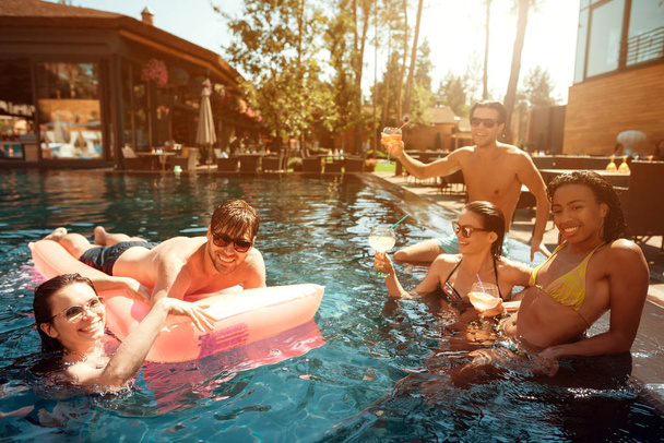 Multiethnic company of people in swimming pool. Company of young people spend weekend in pool. Guys and girls are resting at summer time. - Photo, Image