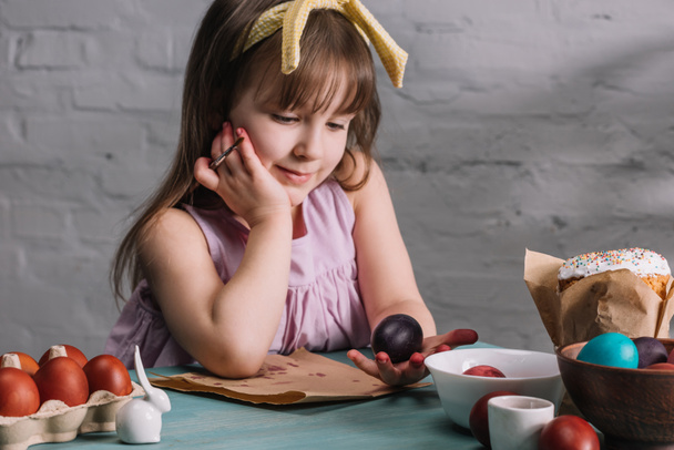 schattig kind kijken naar beschilderde ei in de hand, Pasen concept - Foto, afbeelding