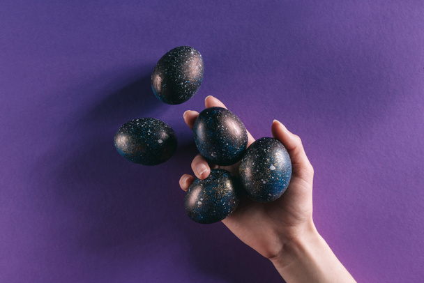 cropped image of woman holding painted easter eggs above violet surface - Fotografie, Obrázek