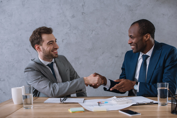 Multicultural business partners shaking hands at working table with documents  - Photo, Image