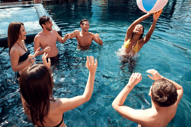 Group of young people play beach ball in pool. Company of friends are having fun in swimming pool. Summer vacation friends together at swimming pool. - Valokuva, kuva