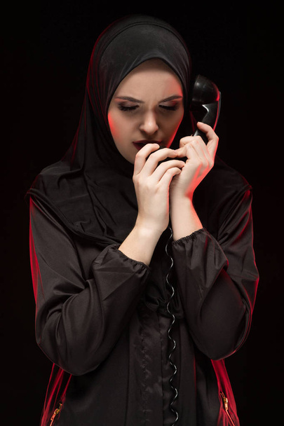 Porträt einer jungen muslimischen Frau mit geschlossenen Augen, die ein Handy in der Hand hält - Foto, Bild