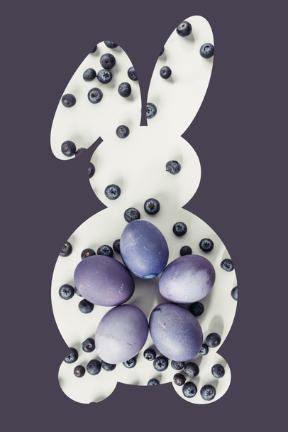 Osterhasen-Symbol mit bemalten Eiern und Blaubeeren isoliert auf violett - Foto, Bild