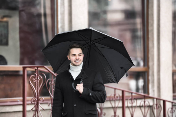 Young man in warm clothes with dark umbrella outdoors - Foto, immagini