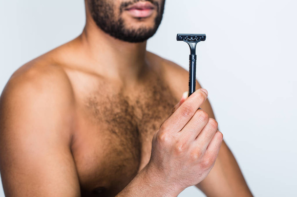 Golić czy nie golić? Częścią przystojny shirtless młody czarny człowiek ogląda razor stojąc na białym tle - Zdjęcie, obraz