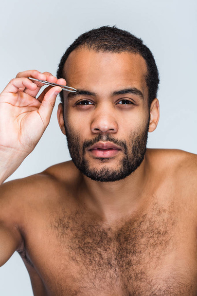 Pampering czas. Portret przystojny shirtless młody czarny człowiek patrząc na kamery i pampering jego brwi, stojąc na białym tle - Zdjęcie, obraz