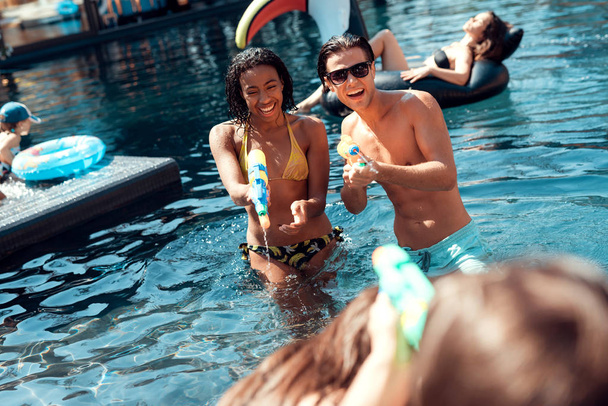 Swimming pool party. Happy people are having fun in swimming pool at summertime. Multiethnic company of friends in swimming pool. - Photo, Image