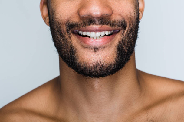 Весела посмішка. Крупним планом частина красивого молодого чорного чоловіка посміхається, стоячи на білому тлі
 - Фото, зображення