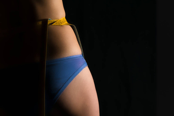 Girl in panty with centimeters on a waist on a black background - Фото, изображение
