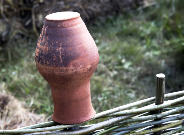 Um jarro de barro antigo em uma cerca de vime
. - Foto, Imagem