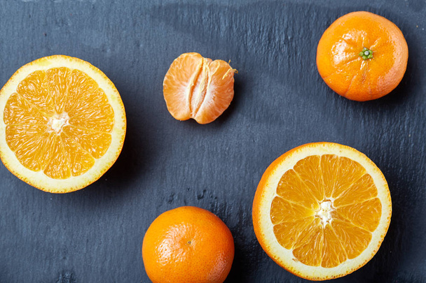 Flat lay of whole and half cut fresh tangerine and orange on dark background, close-up - Foto, afbeelding