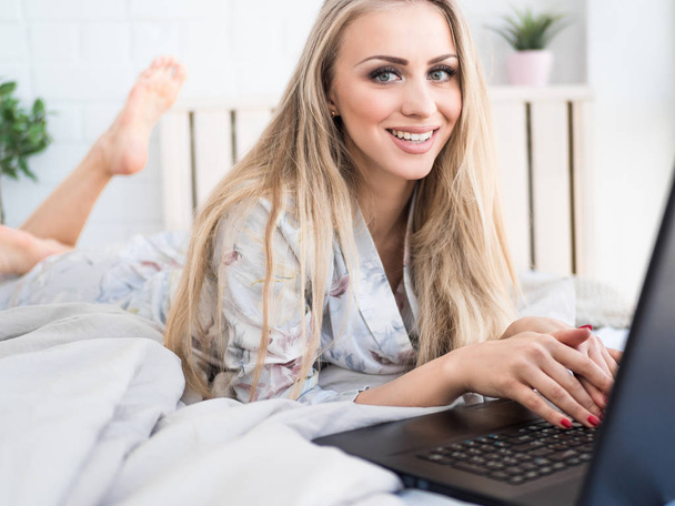 Kobieta przy użyciu komputera przenośnego, leżąc na łóżku. Zbliżenie portret szczęśliwy piękna dziewczyna, wpisując na klawiaturze notebooka - Zdjęcie, obraz