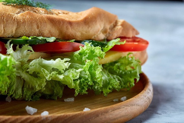 Fresh sandwich with lettuce, tomatoes and cheese served on wooden plate over white textured background, selective focus - Foto, imagen