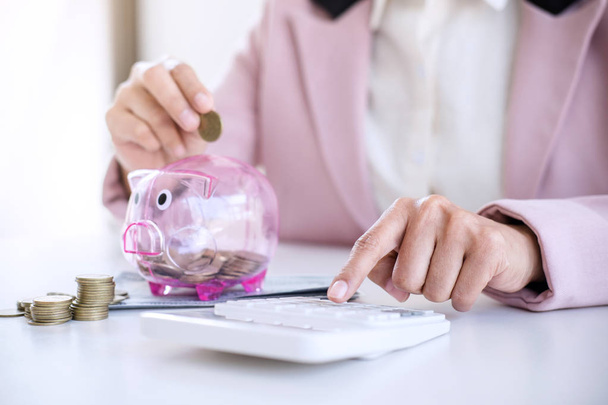 Business woman putting coins into piggy bank and using calculato - Foto, imagen