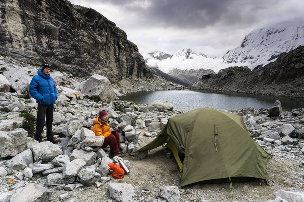 pareja de montañistas masculinos y femeninos en un remoto campamento base en la Cordillera Blanca en Perú junto a un pequeño lago de montaña
 - Foto, imagen