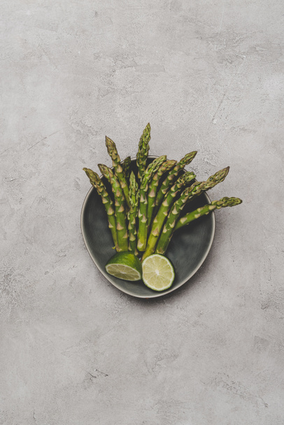 bovenaanzicht van verse gezonde asperges en gesneden kalk op plaat op grijs - Foto, afbeelding