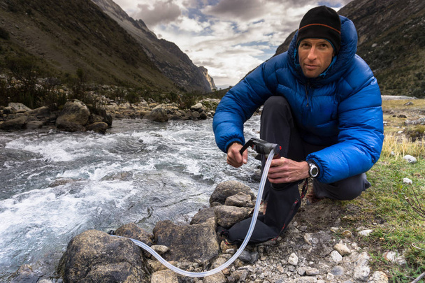 мужчина турист в синей куртке фильтрует питьевую воду из горного ручья в Кордильере Бланка в Андах в Перу
 - Фото, изображение