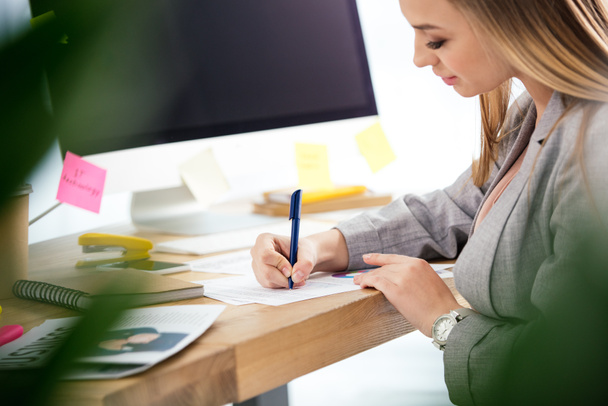 боковой вид женщины-менеджера по маркетингу, выполняющей бумажную работу на рабочем месте в офисе
 - Фото, изображение