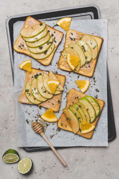 top view of healthy sandwiches with slices of apple and orange, lime and honey dipper on grey   - Foto, Imagen