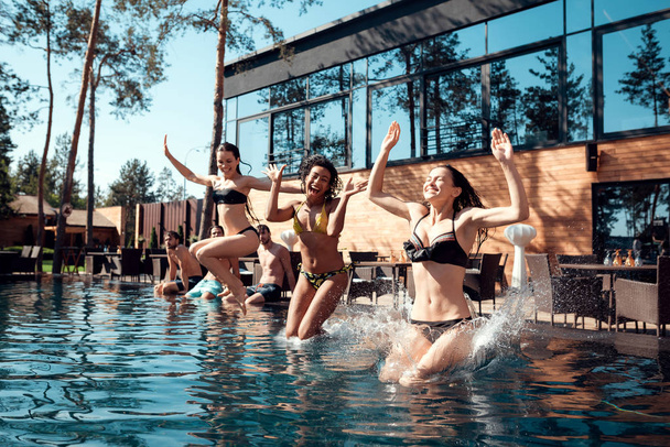 Joyful young girls in swimsuits jumping into pool. Friends carefree spend time near water. Guys and girls are resting on pool. - Photo, Image
