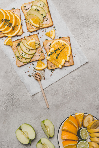 top view of healthy sandwiches with fresh fruits and honey dipper on grey  - Fotó, kép