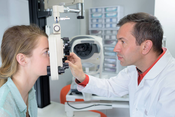 Optometrist aligning equipment to patient's face - Photo, Image