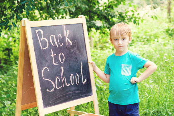 Cute little boy writting on blackboard outdoor . Back to school concept. - Foto, Imagen