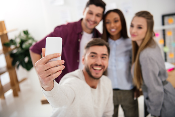 selective focus of happy multicultural business people taking selfie on smartphone together in office - 写真・画像