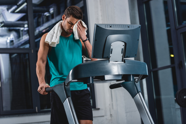tired sweaty sportsman with towel training on treadmill in gym - Fotó, kép