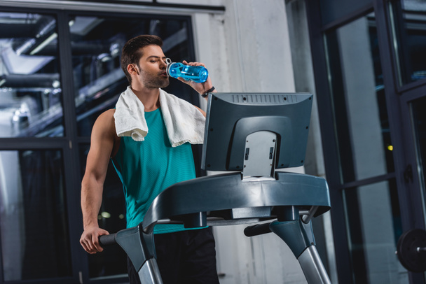 tired sportsman with towel drinking water while training on treadmill in gym - Photo, Image
