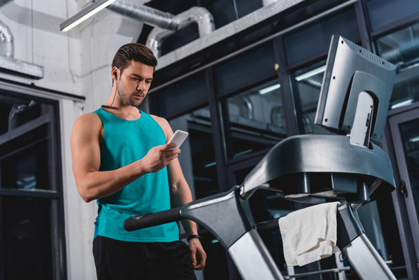Sportsman hallgat zenét a fülhallgató és a smartphone a futópadon a tornateremben edzés közben - Fotó, kép