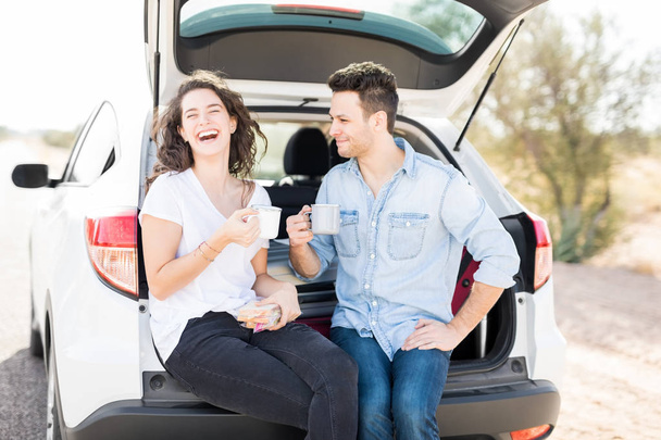 woman laughing while having coffee with her boyfriend inside car trunk - Photo, Image