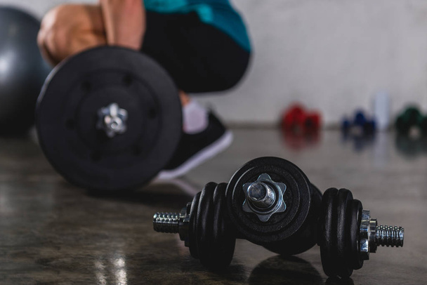 sportsman training with barbell, dumbbells lying on floor on foreground - Foto, imagen