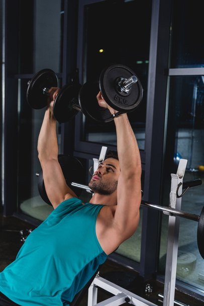 muscular sportsman exercising with dumbbells in gym - Foto, afbeelding