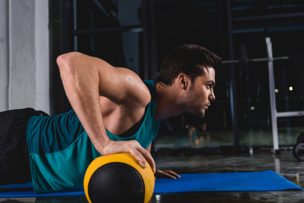 sportsman doing push ups with medicine ball on mat in sports hall - Foto, imagen