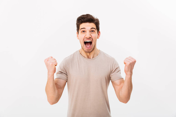 Photo of delighted brunette guy shouting and clenching fists lik - Foto, afbeelding