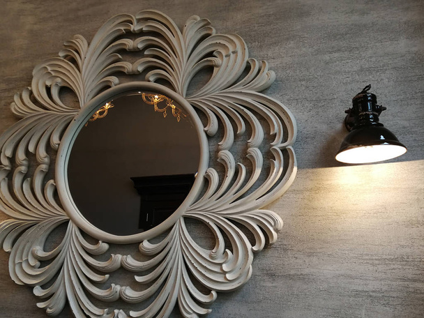 Ένα στρογγυλό καθρέφτη σε ένα διάτρητο πλαίσιο και μια λάμπα στον τοίχο. - Φωτογραφία, εικόνα