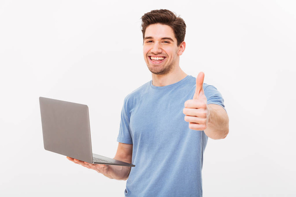 Photo of smiling man in casual t-shirt holding silver laptop and - Foto, Imagen