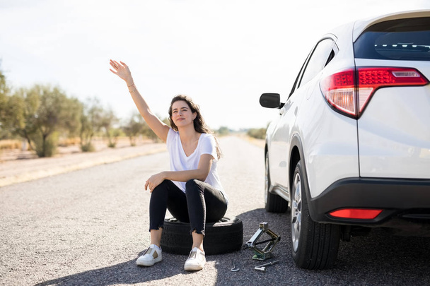 young woman sitting on spare tire on road  - Photo, Image