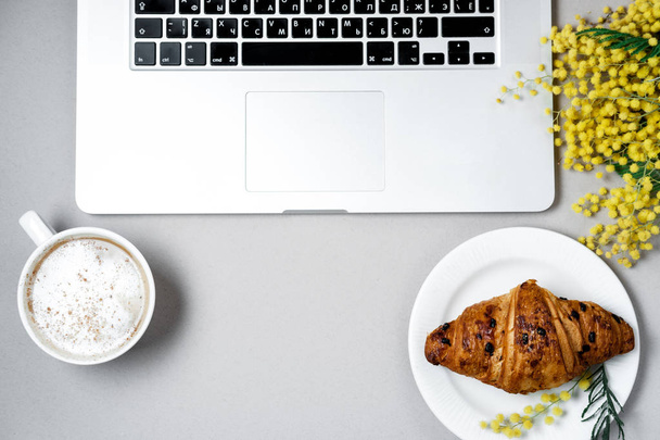 Woman work space with laptop, mimosa flower, croissant, coffee a - Foto, afbeelding