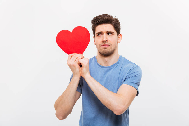 Image of Worried man in t-shirt holding paper heart - 写真・画像