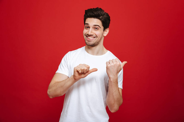 Портрет щасливого молодого чоловіка в білій футболці, що вказує
 - Фото, зображення