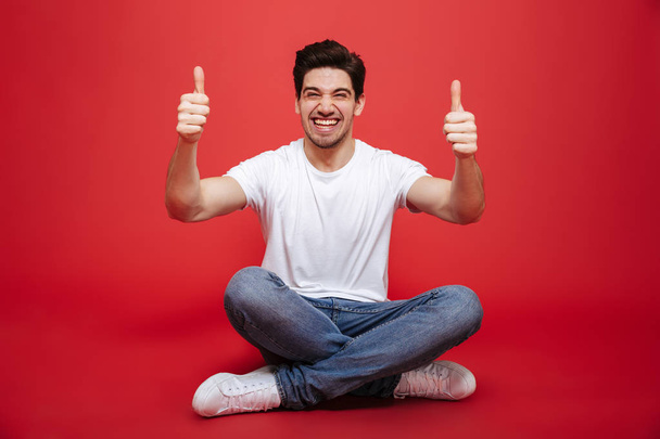 Portrait of a cheerful young man in white t-shirt sitting - Фото, зображення