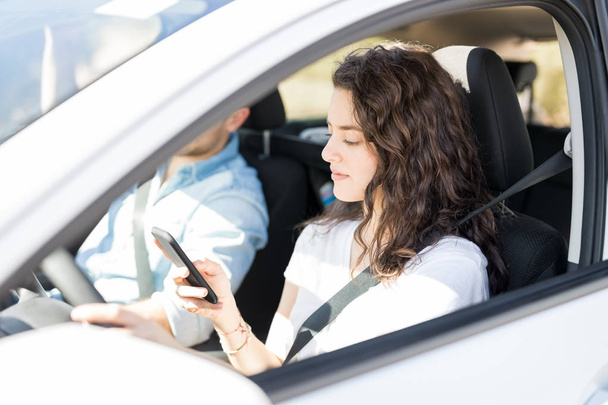 erkek arkadaşı ile araba sürüş sırasında akıllı telefon kullanan genç kadın - Fotoğraf, Görsel