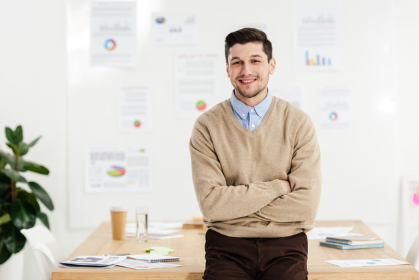 πορτρέτο του χαμογελώντας διευθυντής μάρκετινγκ με τα χέρια σταυρωμένα κλίνοντας στο χώρο εργασίας στο γραφείο - Φωτογραφία, εικόνα
